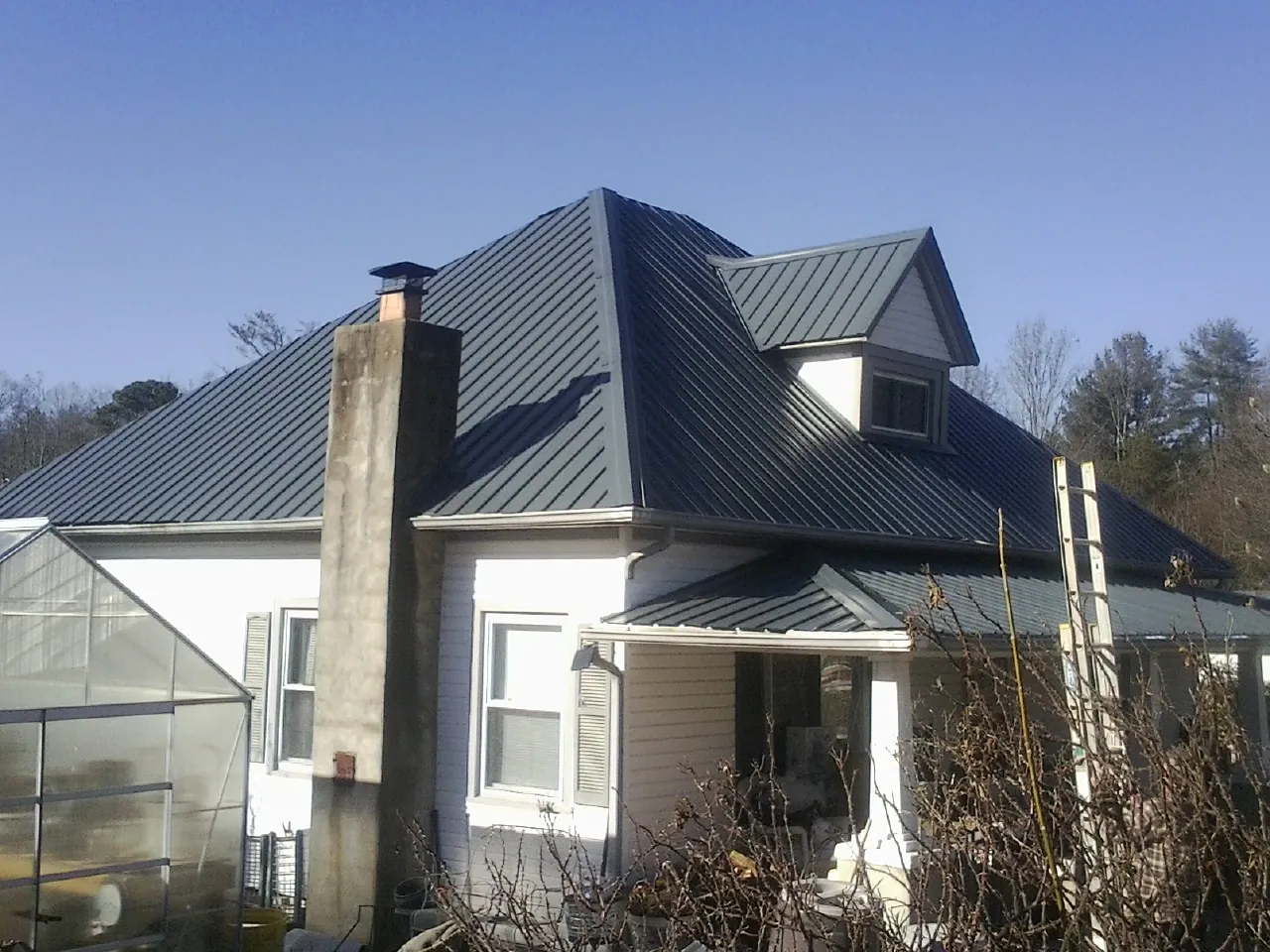 Dark blue standing seam metal roof on a white farmhouse with dormer — Slate & Tile Roof Repair by Roofing Brothers in Cashion
