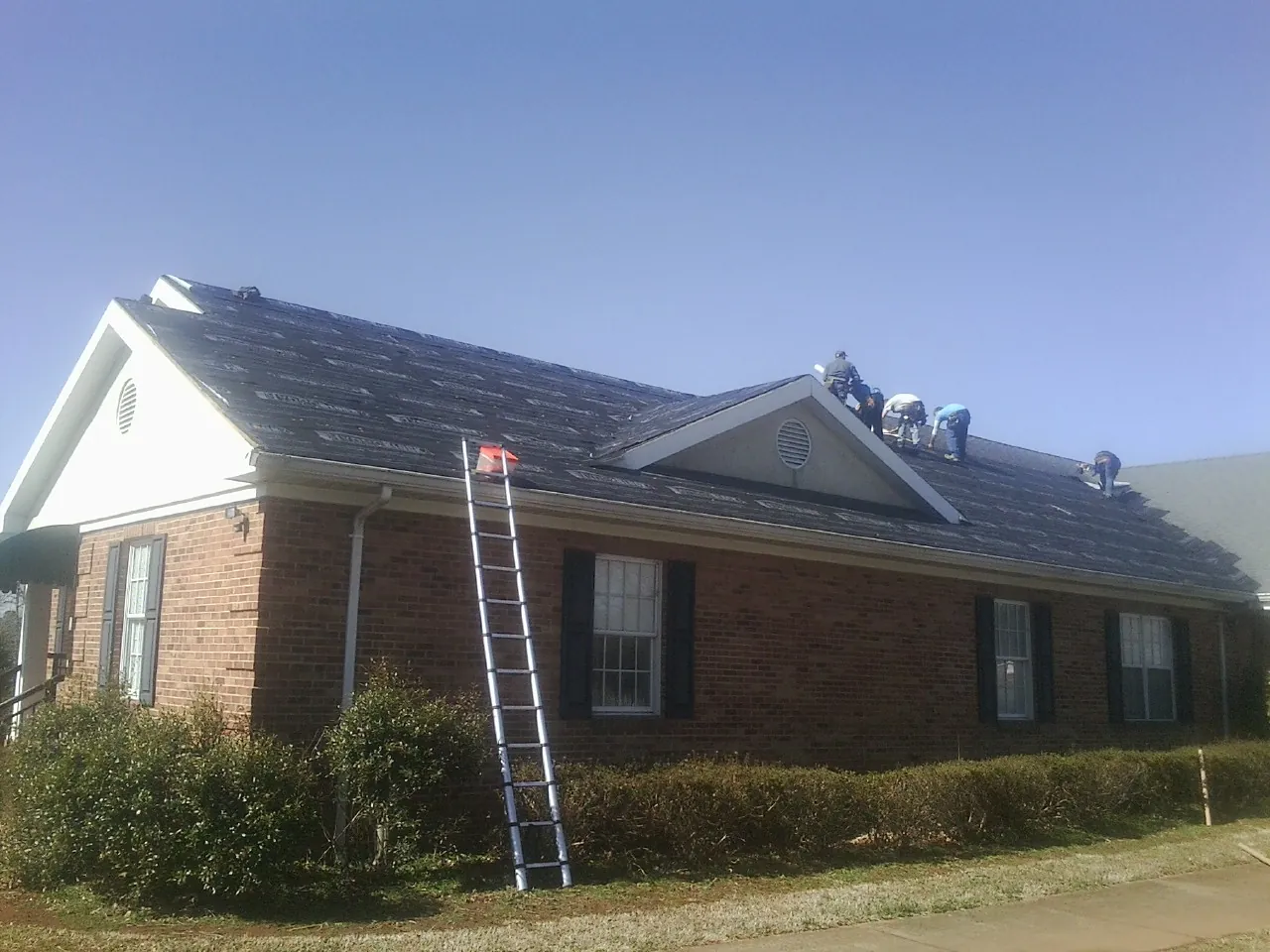 Crew tearing shingles off a brick ranch roof with a ladder set — Metal Roof Repair work by our crew in Cashion