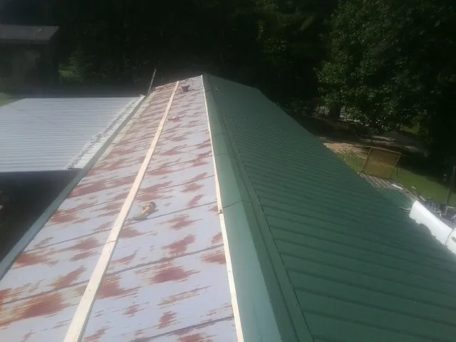 Old rusted panels beside newly installed green metal roofing — Wind Damage Roof Repair by Roofing Brothers in Cashion