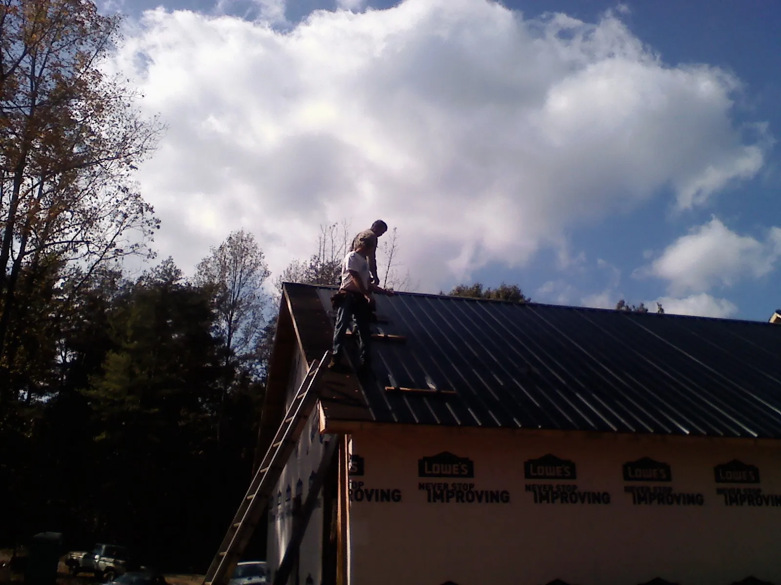 Roofer fastening dark metal panels high against a cloudy sky, from a Roof Inspection job in Cashion